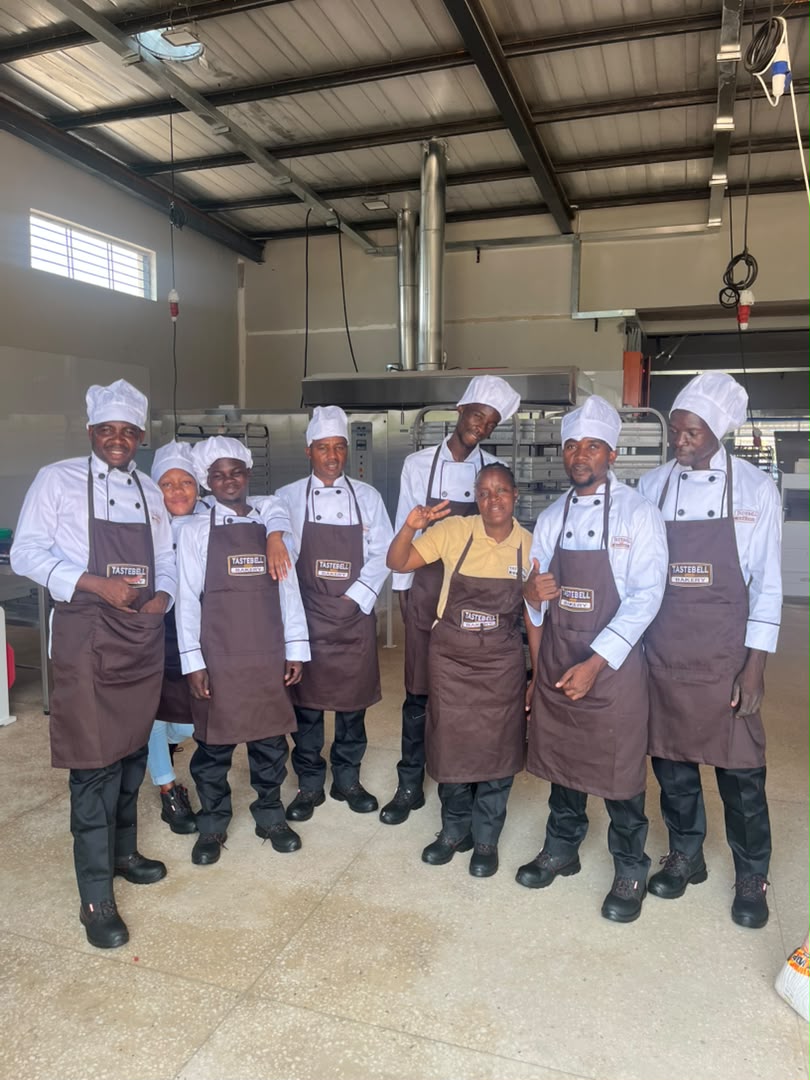 The Tastebell team in chef whites and branded aprons, smiling in the bakery